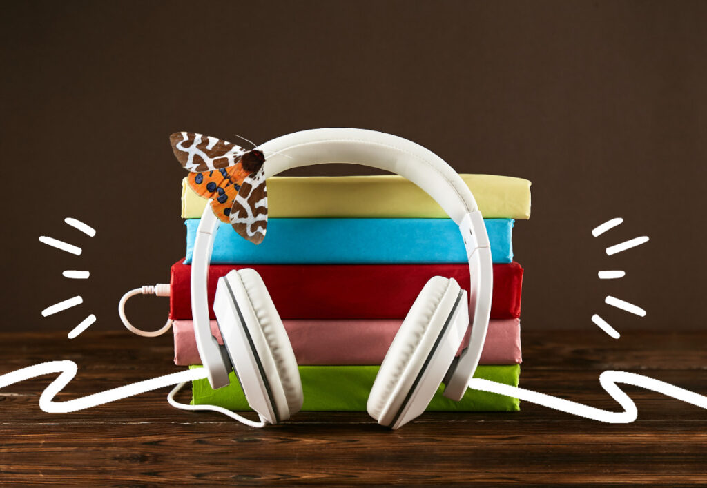 White headphones in front of a stack of books, wrapped in colour paper, recalling a rainbow